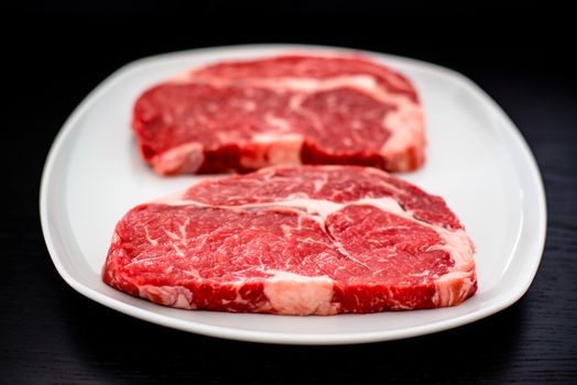 two delicious entrecote steaks on a white plate with dark wooden table in the background - shallow depth of field