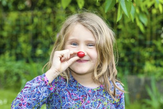 Child with cherry in the hand in a garden