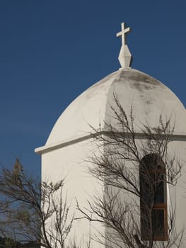 Small white chapel by a tree with blue sky