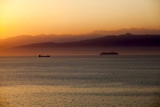 A beautiful Mediterranean sunset with a cruise ship with mountains in the background.