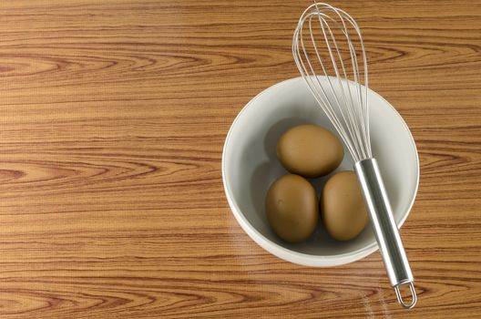 whisk and egg in white bowl on wood table background