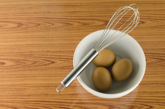 whisk and egg in white bowl on wood table background