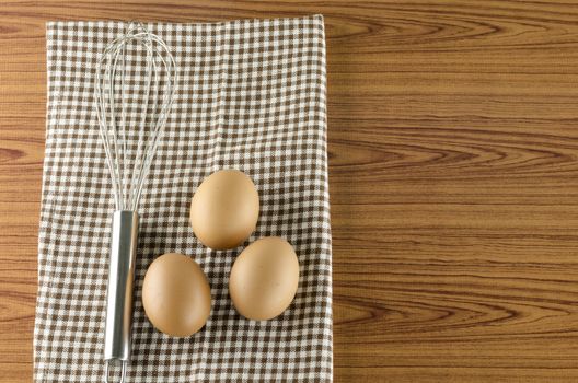 whisk egg and brown kitchen towel on wood table background