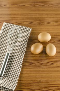 whisk egg and brown kitchen towel on wood table background