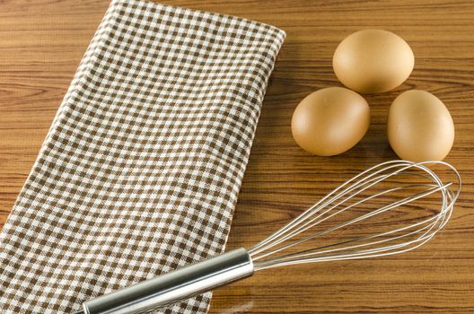 whisk egg and brown kitchen towel on wood table background