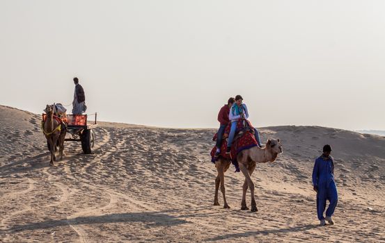 Tourists have the option of riding camels or travelling in a camel drawn cart visiting the sand dunes in Jaisalmer, Rajasthan, India where the Thar Desert begins. Evening time rides offer a chance to see the sunset over the desrt.