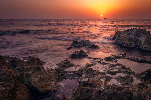 red sunset over the sea with rocks in foreground