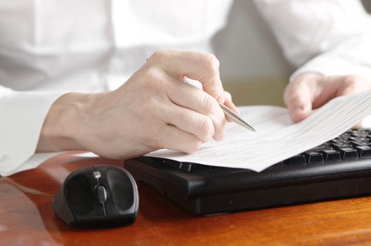 Hands with a document and a pen on a computer keyboard