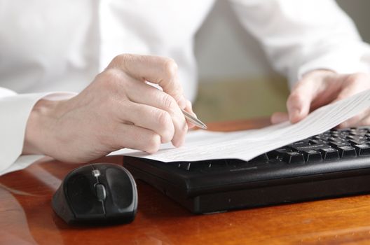 Hands with a document and a pen on a computer keyboard