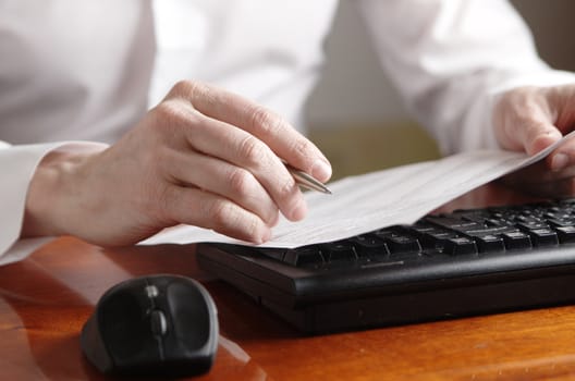 Hands with a document and a pen on a computer keyboard