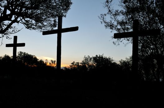 Silhouette of three crosses and trees at sunset
