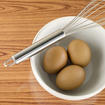 whisk and egg in white bowl on wood table background