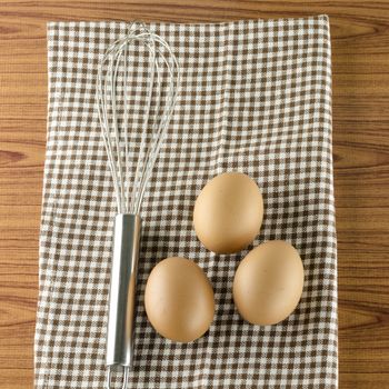 whisk egg and brown kitchen towel on wood table background