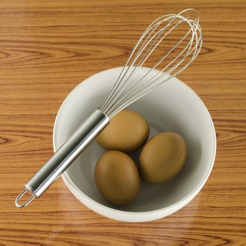 whisk and egg in white bowl on wood table background