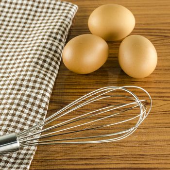 whisk egg and brown kitchen towel on wood table background