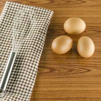 whisk egg and brown kitchen towel on wood table background