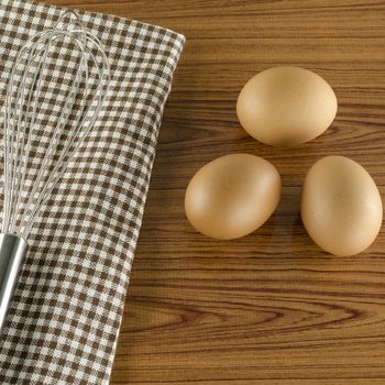 whisk egg and brown kitchen towel on wood table background