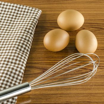 whisk egg and brown kitchen towel on wood table background