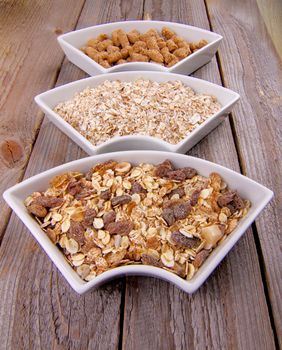 Arrangement of Muesli, Oat Flakes and Bran in White Bowls on Rustic Wooden background