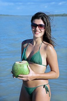 beautiful smiling bikini dressed young Brazilian woman drinking and holding fresh coconut juice in the tatajuba lagoon in jericoacoara ceara state near fortaleza