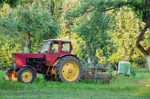 rustic old farm tractor with yellow wheels and harow in garden grass