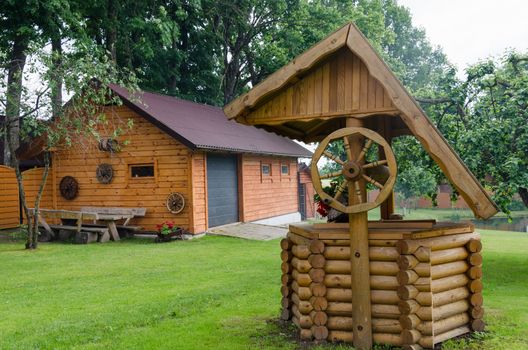 Rural well manhole decoration and house made of wooden logs in country homestead.