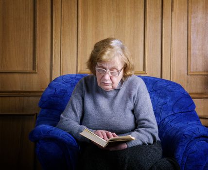 The old woman sits in an armchair and reads the book