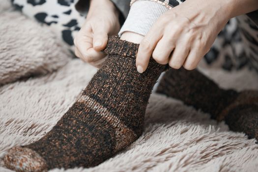 Woman hands putting on warm woolen socks 