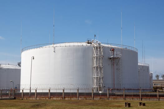 multiple white big oil storage tanks with a fence around them