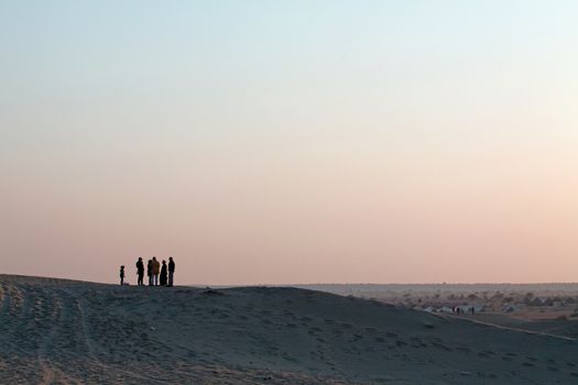 Silhoutte of Group of People with Small Child in Discussion standing on Sand-dunes with Large Expanse of Dusk sky as Background
