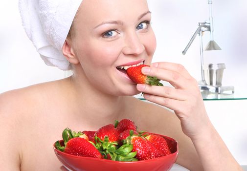 Attractive girl with a bowl of ripe strawberries relaxes in the living room.