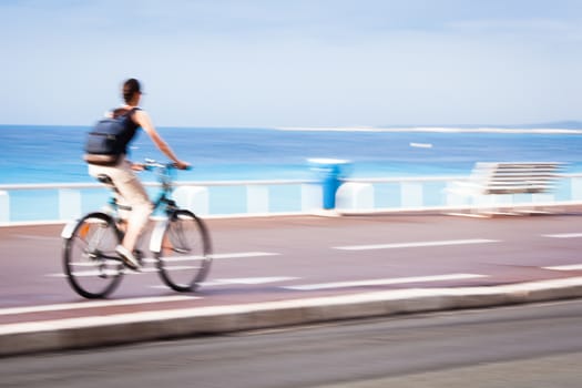 Great way to get around in a city -Motion blurred cyclist going fast on a city bike lane, by the sea shore