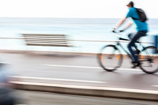 Great way to get around in a city -Motion blurred cyclist going fast on a city bike lane, by the sea shore