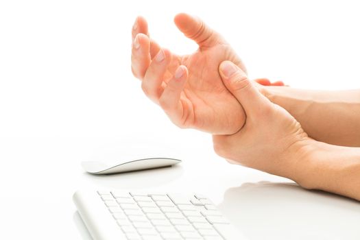 Working too much - suffering from a Carpal tunnel syndrome - young man holding his wrist in pain due to prolonged use of keyboard and mouse over white background (color toned image; shallow DOF)