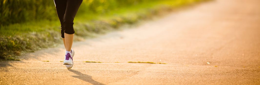 Detail of legs of a female runner on road - jog workout/well-being concept