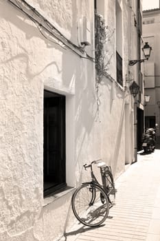 Spanish town street with a bicycle at a white wall, sepia photo