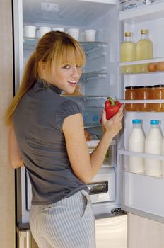 Young woman taking a vegetable from her fridge full with fresh foods