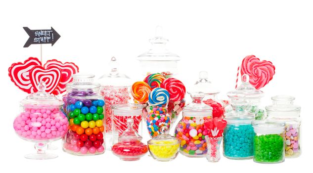 A candy buffet with a wide variety of candies in apothecary jars.  Shot on white background.