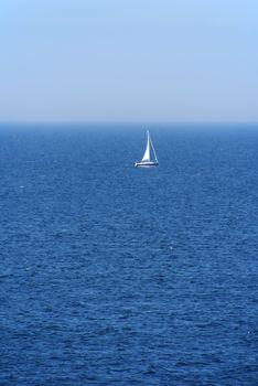 One lonely sailboat on the blue ocean and sky.