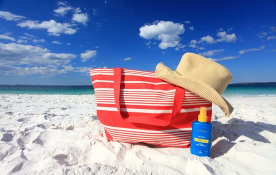 Summer sun protection at the beach, each hat and sunscreen on the sand at he beach.  Logos removed