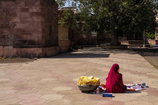 Indian woman in Bright clothes sitting among the ancient monuments of stone in mandore, rajasthan india, selling kitkat and small eats