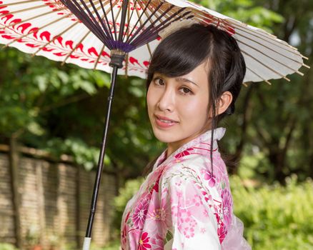 Asian woman in a kimono in a Japanese style garden holding an umbrella