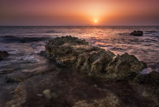 red sunset over the sea with rocks in foreground