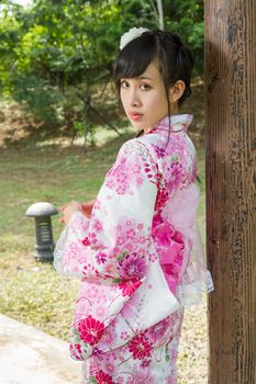 Asian woman in a kimono in a Japanese style garden leaning against pillar