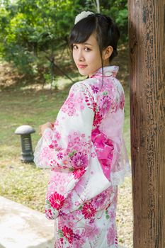 Asian woman in a kimono in a Japanese style garden leaning against pillar