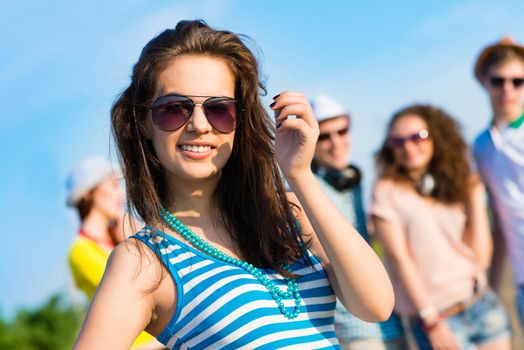 stylish young woman in sunglasses on the background of blue sky and friends
