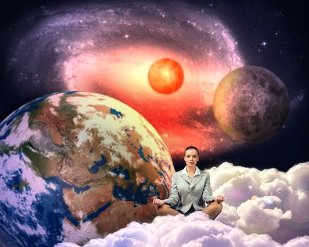 image of a businesswoman meditating in the clouds in space. Elements of this image furnished by NASA