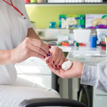 Medical doctor performing a quick prick test for blood group determination by using blood type testing kit with anti A and B antibodies on a white card.