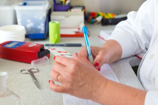 Medical doctor performing a quick blood group determination by using blood type testing kit with anti A and B antibodies on a white card.