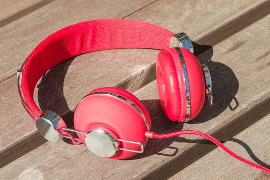 Bright red wired headphones on wooden backyard bench